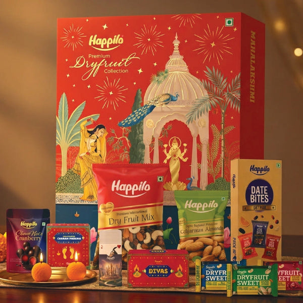 Burgundy and gold Happilo corporate dry fruits gift box beside brass bowls of almonds, cashews, pistachios and green raisins