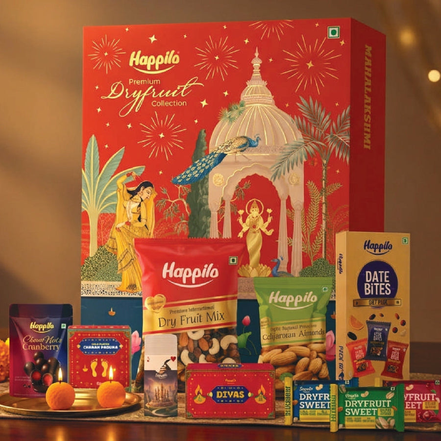 Burgundy and gold Happilo corporate dry fruits gift box beside brass bowls of almonds, cashews, pistachios and green raisins